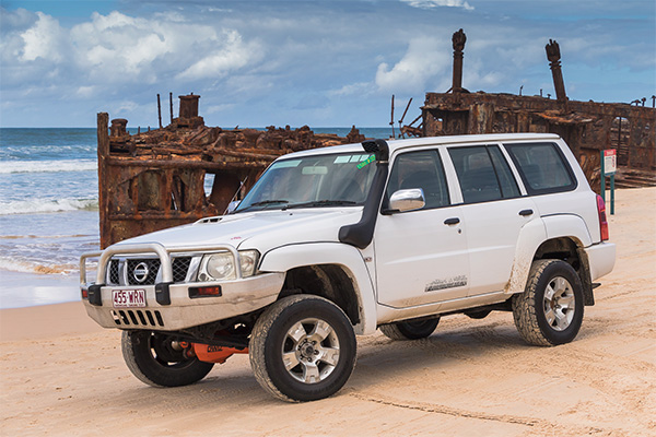 A 4WD on the beach in front of the rusted S.S. Maheno shipwreck on K'gari
