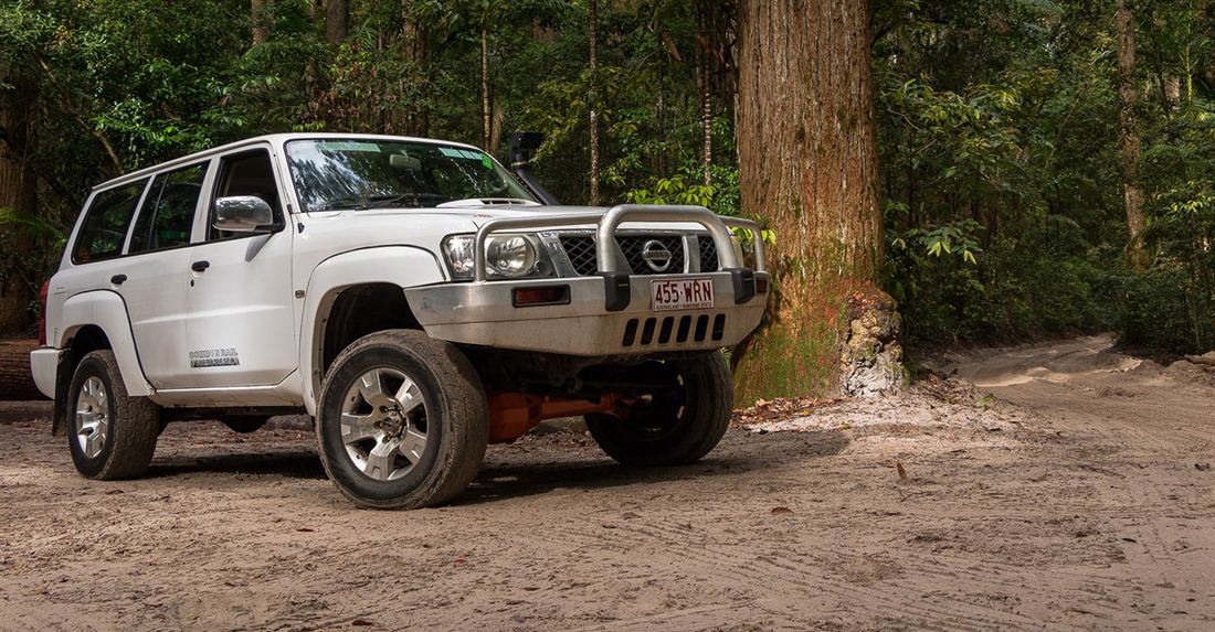 A prepped 4WD parked on the sand beside towering rainforest on K'gari